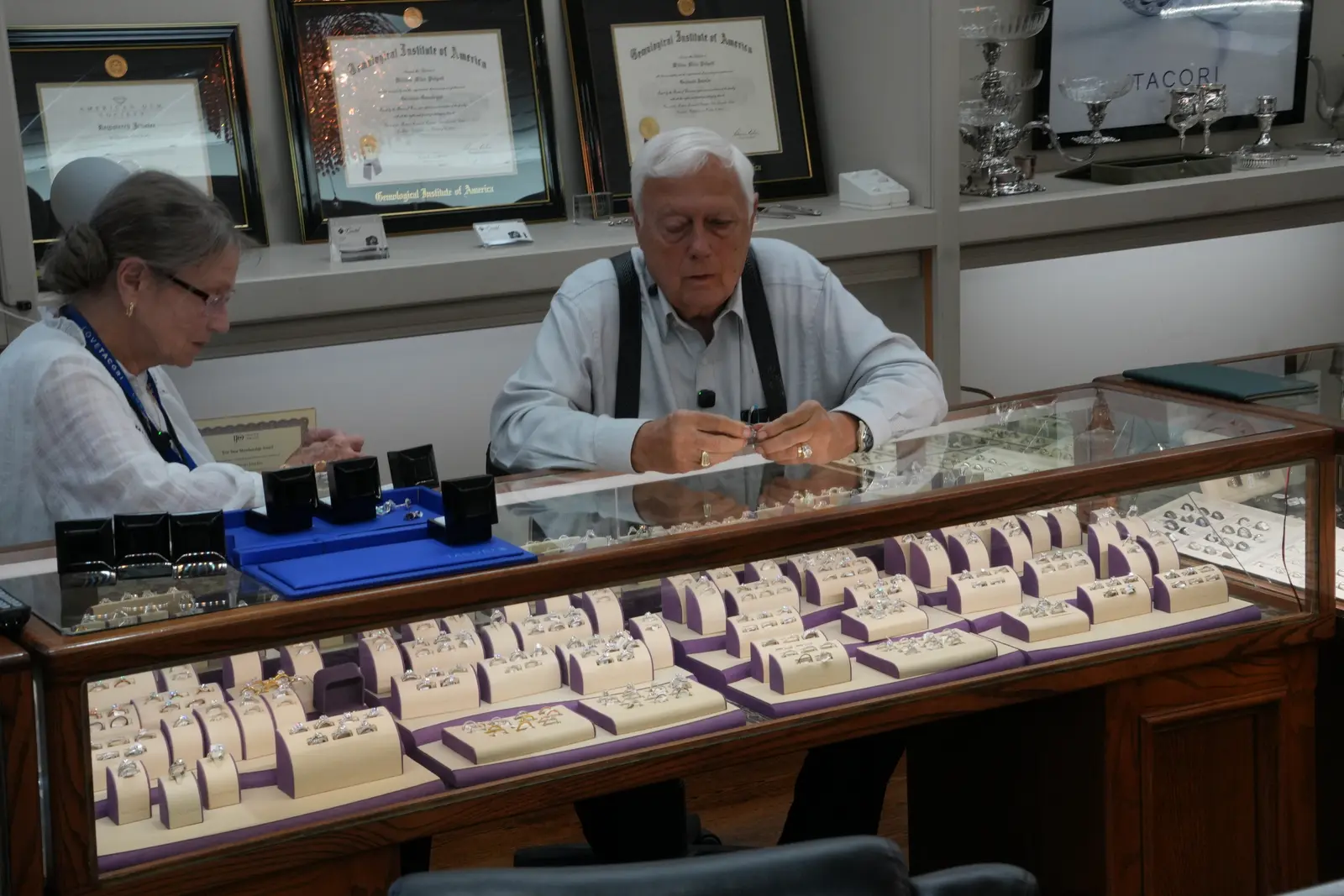 The owners of O'Neal's Jewelers in Pauls Valley, Oklahoma, seated behind a display case of rings during a shoot-day interview, with framed GIA diplomas on the wall behind them
