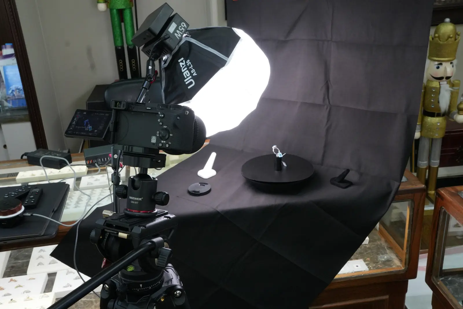 Close view of the camera and tripod pointed at a ring on the turntable, with the softbox lit behind