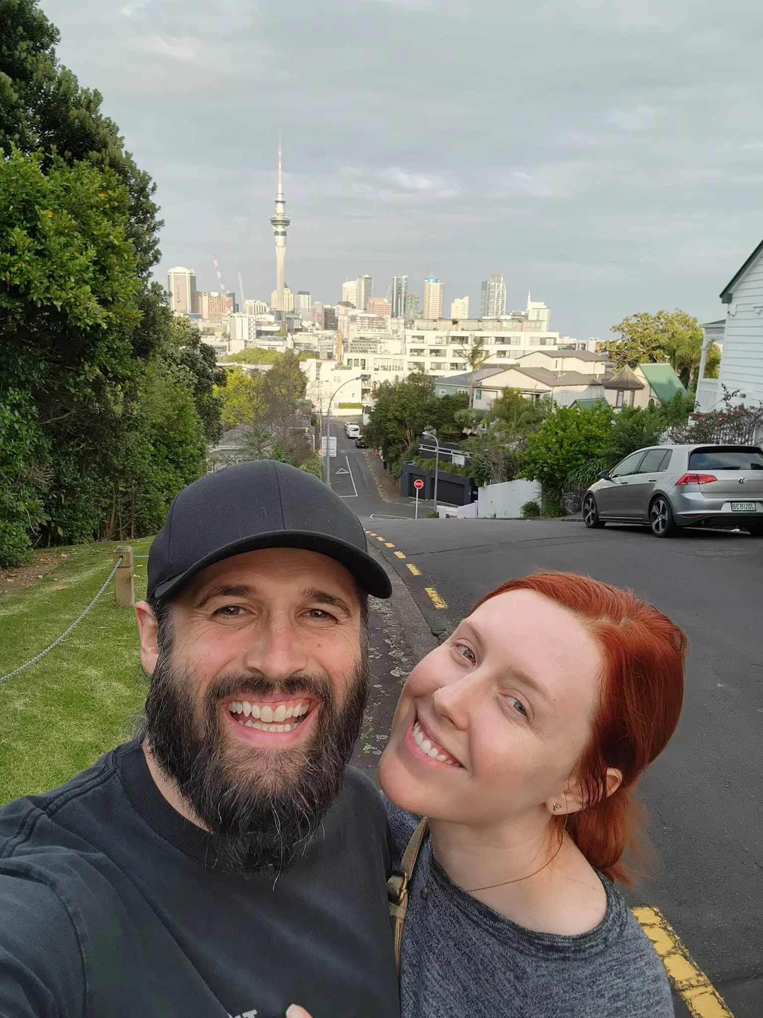Selfie of Mitch in a black cap and Brittany, with a city skyline and a tall tower behind them