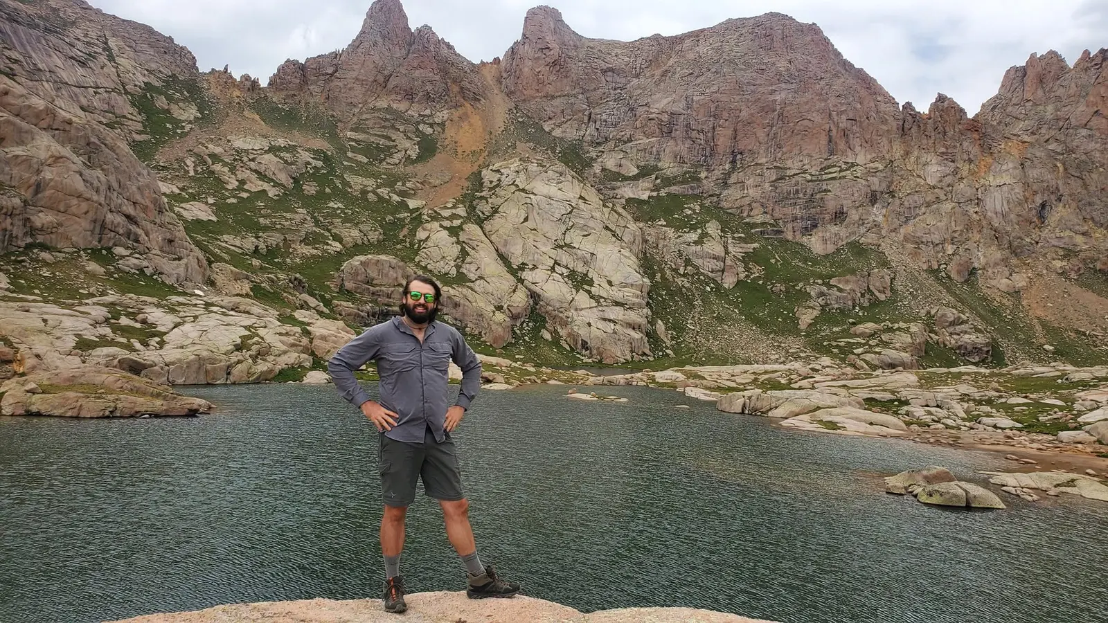 Mitch standing on a rock beside an alpine lake below red cliffs