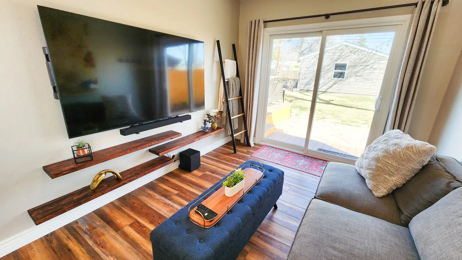 The Elati House living room with a gray sectional, a navy ottoman and a wall-mounted TV